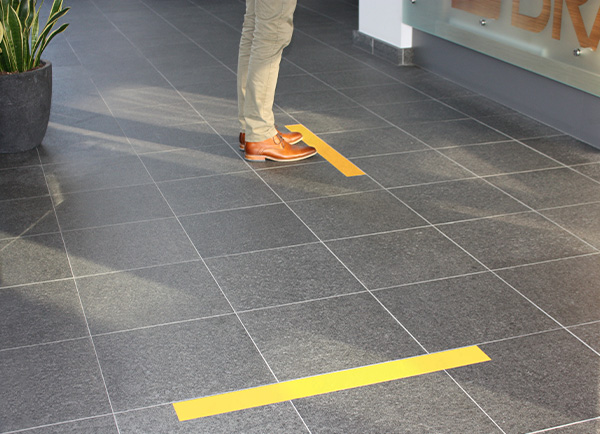 A person is using their hands to remove ToughStripe Vinyl floor tape from vinyl composition tile. The tape is coming off cleanly in one piece.