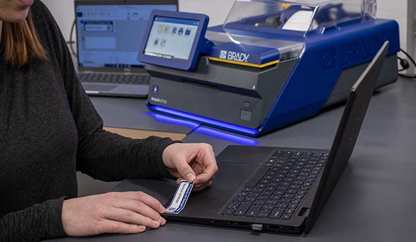 A worker applies an asset tag to a laptop.