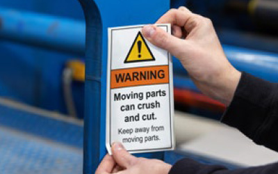 A person puts a pinch point warning label on a machine.