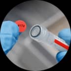 A red label with printed text being applied to the top of a tube with a corresponding colour.