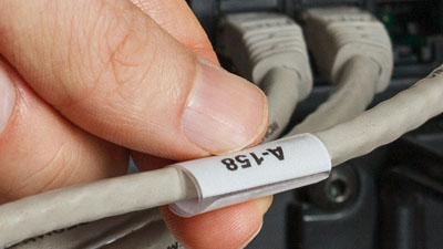A hand grabbing a white identification label looped around a gray cable.