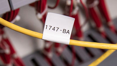 A white cloth label identifying a yellow cable withing a piece of industrial equipment.