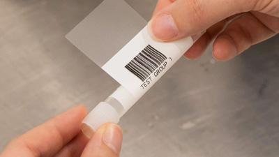 A person wraps a vial with a self-laminating barcode label.