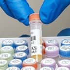 A lab technician holding a test tube with two barcode labels.